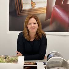 Artist seated at a table reviewing photographic prints, with framed artwork displayed on the wall behind.
