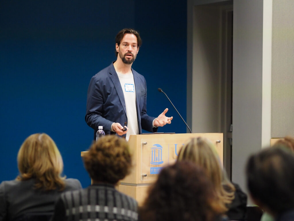Dr. Timothy Hughs presents at the podium during the 4th Annual Duke/UNC ADRC SLAM‑DUNC Symposium.