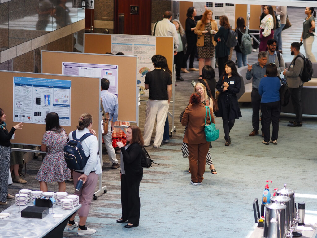 Attendees view research posters during the 4th Annual Duke/UNC ADRC SLAM‑DUNC Symposium in a large indoor atrium.